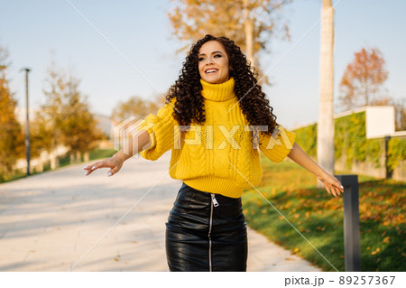 A girl in a bright sweater and leather skirt spread her arms cheerfully laughing on the track of autumn park A girl in a bright sweater and leather skirt spread her arms cheerfully laughing on the track of autumn park 89257367