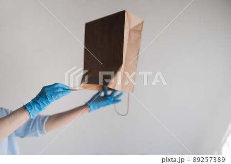 Hands in blue latex gloves shake an empty paper bag trying to get hold of something, against a white background 89257389