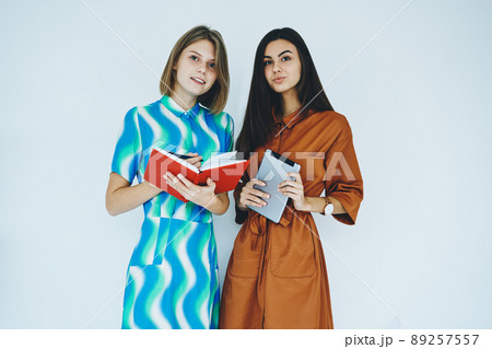 Female friends holding tablet and notebook while standing 89257557