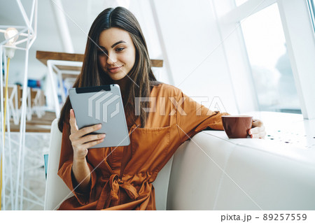 Young woman reading book on tablet and having hot drink in modern office 89257559