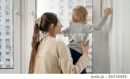 Young mother with her baby son walking out of the window at house Young mother with her baby son walking out of the window at house 89258889