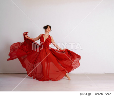 Dancer in a red flying dress. Woman ballerina dancing on a white studio background 89261592