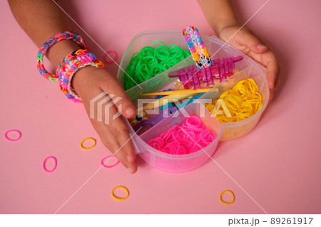 Colored rubber bands for weaving bracelets in a heart-shaped box is held by a child. Fashionable bracelets made of elastic bands on the girl's wrist. tools and machine for manufacturing Colored rubber bands for weaving bracelets in a heart-shaped box is held by a child. Fashionable bracelets made of elastic bands on the girl's wrist. tools and machine for manufacturing 89261917