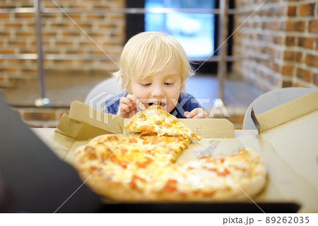 Cute blonde boy eating slice of pizza at fast food restaurant. Hungry child. Unhealthy meal for kids. Junk food. Overweight problem children 89262035