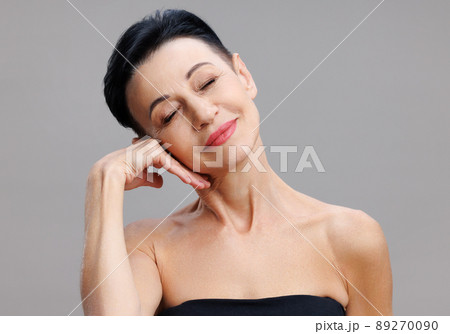 Middle aged woman touching face gainst gray background Middle aged woman touching face gainst gray background 89270090