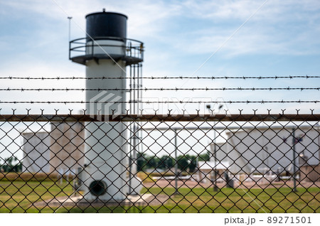 chemical facility security chain fence with barbed wire top in focus and a blurred tank farm and emergency flare in the background 89271501