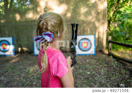 Young girl at summer camp learning to use a bow and arrow looking down field at the target. Young girl at summer camp learning to use a bow and arrow looking down field at the target. 89271506