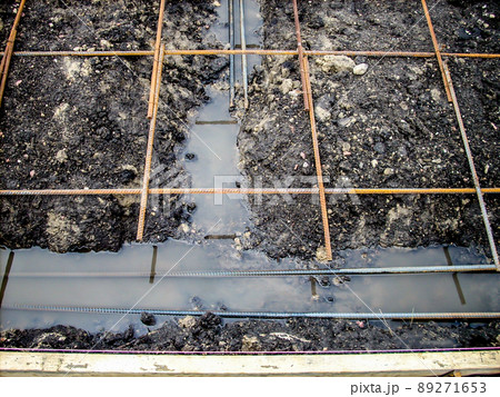 Construction site rebar suspended over a footing trench filled with rain water.  89271653