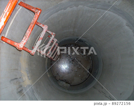 Looking into an open concrete manhole with step rungs leading down stagnant water Looking into an open concrete manhole with step rungs leading down stagnant water 89272156