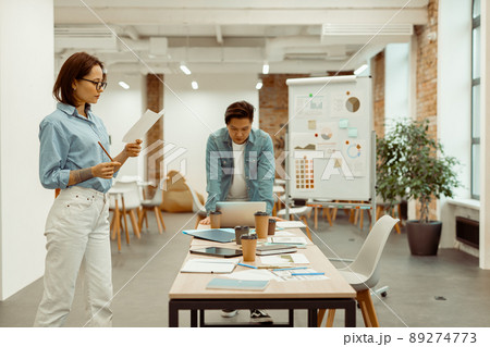 Two colleagues standing in the office and focused on work Two colleagues standing in the office and focused on work 89274773