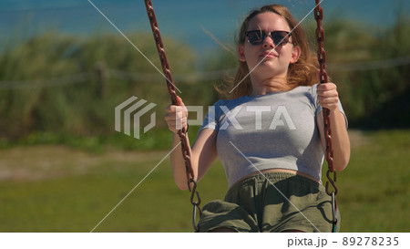 Young pretty woman sits on a swing and enjoys the sun 89278235
