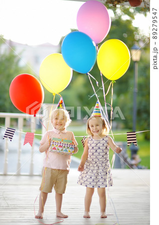 Little boy and girl having fun and celebrate birthday party with colorful balloons. Happy preschiooler child with festive gifts at summer outdoor party Little boy and girl having fun and celebrate birthday party with colorful balloons. Happy preschiooler child with festive gifts at summer outdoor party 89279547