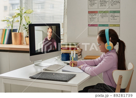 Nerd girl in colorful headphones making notes in workbook and watching online lesson on computer while studying at home Nerd girl in colorful headphones making notes in workbook and watching online lesson on computer while studying at home 89281739