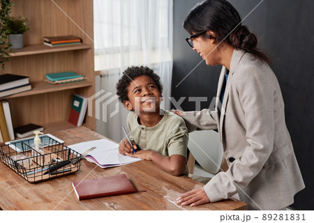 Hispanic tutor in jacket touching shoulder of black boy while supporting him during one-by-one lesson Hispanic tutor in jacket touching shoulder of black boy while supporting him during one-by-one lesson 89281831