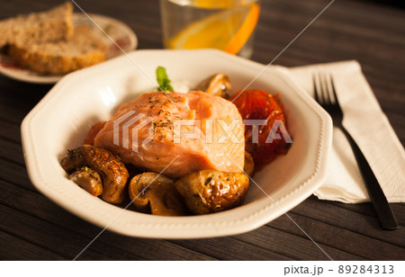 steamed salmon fillet on a pillow of fried mushrooms and tomatoes in a white bowl 89284313