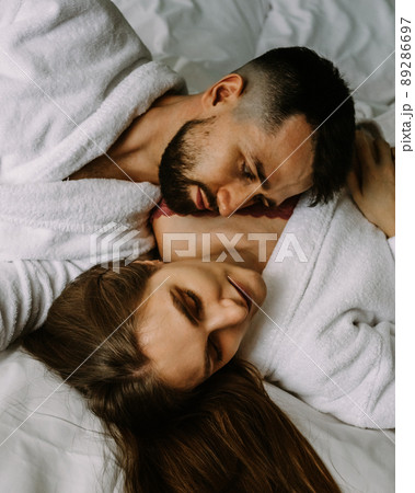 Portrait of young loving couple in bathrobes relaxing on bed at hotel Portrait of young loving couple in bathrobes relaxing on bed at hotel 89286697
