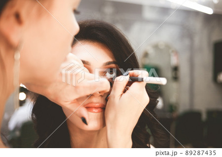 Makeup artist paints eyes with eyeliner. Professional visagiste does makeup to a beautiful lady.. 89287435