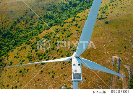 Wind turbine with large propeller generates electricity rotating at station in highland covered with green trees close aerial view 89287802