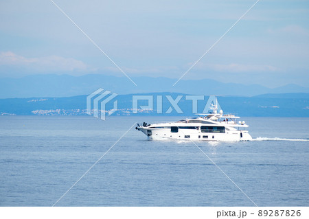 Big tourist motorboat sails on calm Mediterranean sea water against small coastal town near large forestry mountains in sunny morning Big tourist motorboat sails on calm Mediterranean sea water against small coastal town near large forestry mountains in sunny morning 89287826