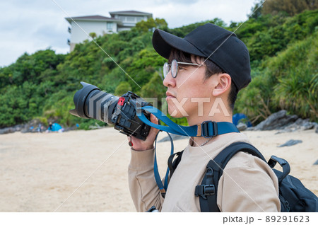 南国の砂浜で、一眼レフカメラで楽しく撮影する若い男性 89291623