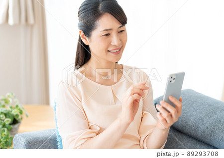 部屋でスマホを操作するミドル女性 89293708