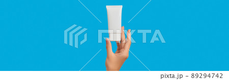 Womans hand with blue manicure holding white tube. Care products Womans hand with blue manicure holding white tube. Care products 89294742