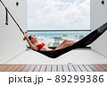 Back view of woman in red bikini resting in hammock with ocean view on rooftop of a luxury hotel. 89299386