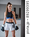 Portrait of a young attractive girl boxer in the gym wearing gloves next to a punching bag 89299395