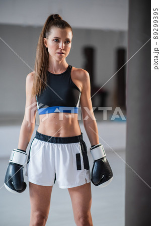 Portrait of a young attractive girl boxer in the gym wearing gloves next to a punching bag Portrait of a young attractive girl boxer in the gym wearing gloves next to a punching bag 89299395
