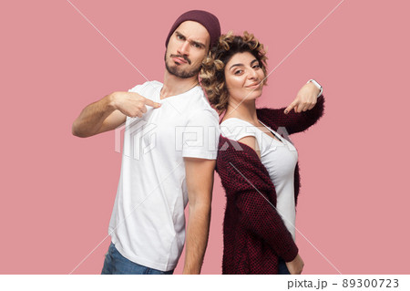Portrait of satisfied successful couple of friends in casual style standing back to back, pointing themself with proud face and looking at camera. Isolated, indoor, studio shot, pink background Portrait of satisfied successful couple of friends in casual style standing back to back, pointing themself with proud face and looking at camera. Isolated, indoor, studio shot, pink background 89300723