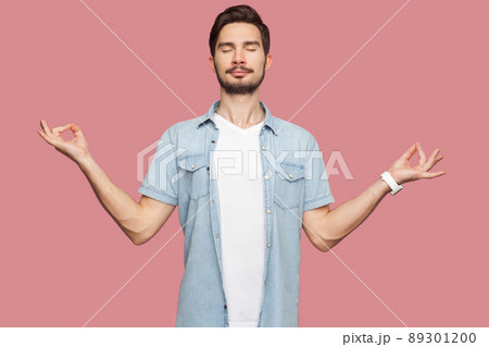 Portrait of calm relaxed handsome bearded young man in blue casual style shirt standing with raised arms and doing yoga meditating exercise. indoor studio shot, isolated on pink background. Portrait of calm relaxed handsome bearded young man in blue casual style shirt standing with raised arms and doing yoga meditating exercise. indoor studio shot, isolated on pink background. 89301200