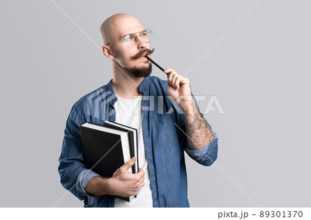 Portrait of thoughtful handsome guy student who holds books and pen. Concept of brainstorming. 89301370
