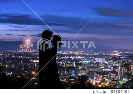花火大会でプロポーズが成功したイメージ。花火と夜景をバックにキスするカップル。 89304409