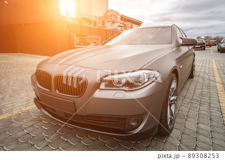 Predatory car headlight with blue lights and hood of powerful grey blue car sports car with matte grey paint and wheel with blue disc Predatory car headlight with blue lights and hood of powerful grey blue car sports car with matte grey paint and wheel with blue disc 89308253