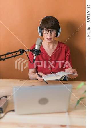 Portrait of mature woman wearing headphones and talking at online radio station - podcast and broadcast concept 89310117