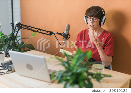 Portrait of mature woman wearing headphones and talking at online radio station - podcast and broadcast concept 89310122