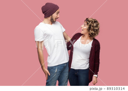 No way. Portrait of excited couple of friends in casual style standing and looking to each other with amazing faces, big eyes and toothy smile. Isolated, indoor, studio shot, pink background 89310314