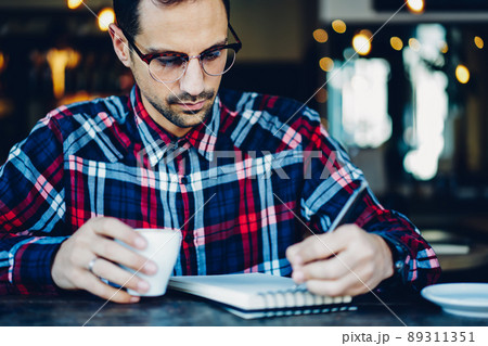 Young blogger holding coffee cup and using notepad for noting some memo records Young blogger holding coffee cup and using notepad for noting some memo records 89311351