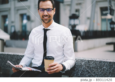 Portrait of happy businessman in optical spectacles holding newspaper and coffee cup Portrait of happy businessman in optical spectacles holding newspaper and coffee cup 89311420