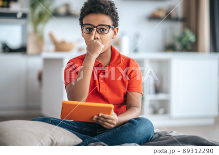 A boy in orange tshirt touching his eyewear and looking serious A boy in orange tshirt touching his eyewear and looking serious 89312290