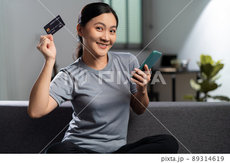 Asian woman sitting on sofa using smart phone and credit card for shopping online at home. Asian woman sitting on sofa using smart phone and credit card for shopping online at home. 89314619