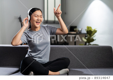 Happy woman with headphones and listening to music sitting on sofa at home. 89314647