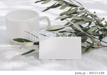 Summer wedding stationery mock-up scene. Blank business card, invitation. Green olive branch and blurred cup of coffee, tea in sunlight. White linen tablecloth background. Mediterranean,Italian design Summer wedding stationery mock-up scene. Blank business card, invitation. Green olive branch and blurred cup of coffee, tea in sunlight. White linen tablecloth background. Mediterranean,Italian design 89315199