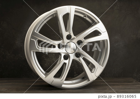 new grey alloy wheels on a dark textured black background. a wheel for a car 89316065