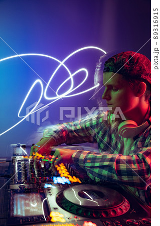 Portrait of young boy in casual cloth, party dj making music with professional sound mixer isolated over purple background in neon light 89316915