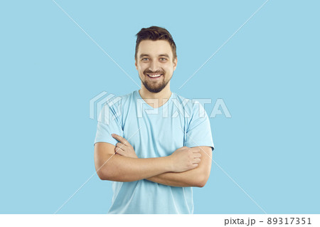 Happy handsome young man in a blue T shirt standing with his arms crossed and smiling Happy handsome young man in a blue T shirt standing with his arms crossed and smiling 89317351