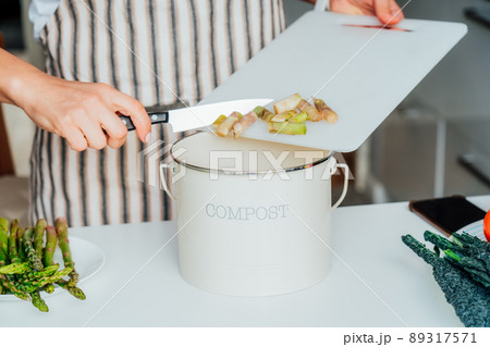 Compost the kitchen waste, recycling. Household woman scraping, throwing vegetables cutting leftovers into the garbage, compost bin while cooking on her kitchen. Environmentally responsible, ecology. 89317571