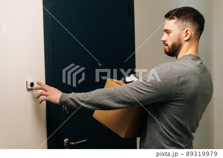 Delivery man holding cardboard box and contactless payment POS wireless terminal for card paying and ringing doorbell of customer apartment. Concept of online shopping. Delivery man holding cardboard box and contactless payment POS wireless terminal for card paying and ringing doorbell of customer apartment. Concept of online shopping. 89319979