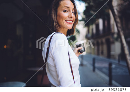 Smiling female looking at camera holding disposable cup in town Smiling female looking at camera holding disposable cup in town 89321073