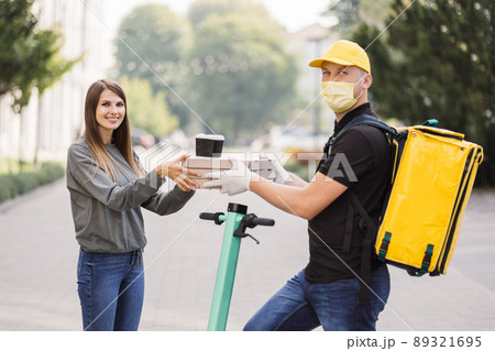 Attractive young delivery guy holding boxes with hot pizza and two cups of hot drink coffee. 89321695